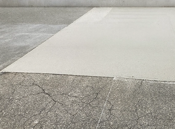 コンクリート舗装（セメントミルク工法）された地面の画像。灰色の地面の一部が滑らかな白いコンクリートで四角く舗装されている。